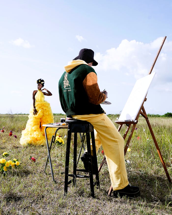 Artist painting a model in a yellow dress outdoors with flowers in Lagos, Nigeria.